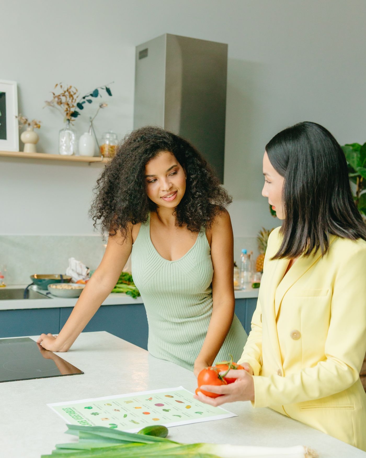 Two women talking through healthy eating together at a kitchen counter with fresh vegetables